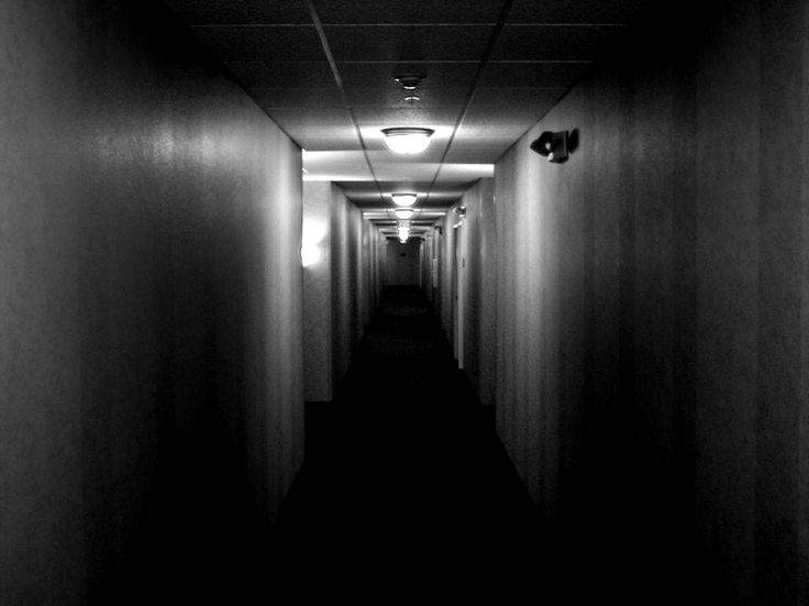 a dark hallway with light at the end and no one in sight on the other side