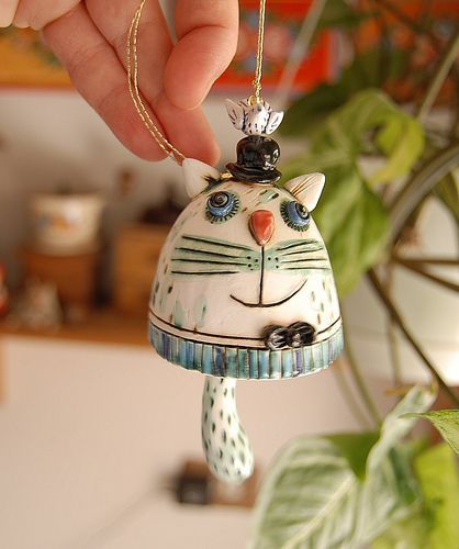 a hand holding a ceramic cat ornament in front of a potted plant