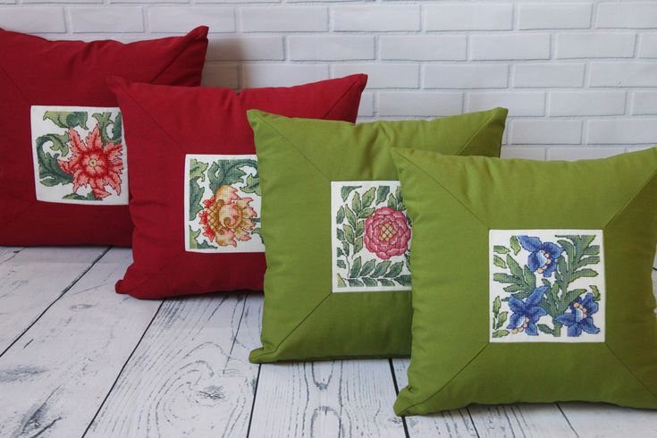 three pillows with different designs on them sitting on a white wooden floor next to a brick wall