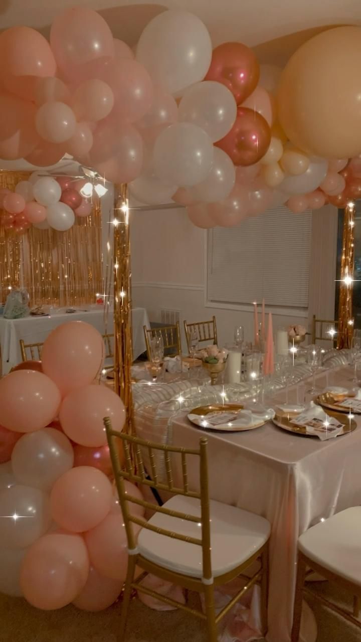 the table is set for a party with pink and white balloons hanging from the ceiling