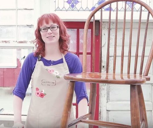 a woman standing next to a wooden chair with an apron on it's back