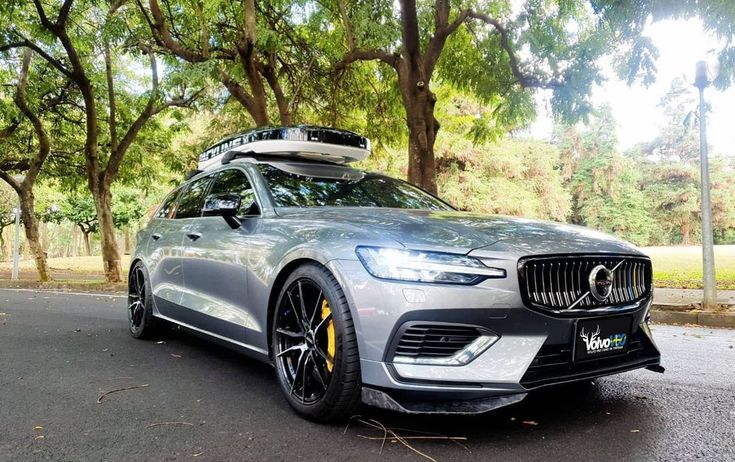 a silver volvo car is parked on the side of the road with trees in the background