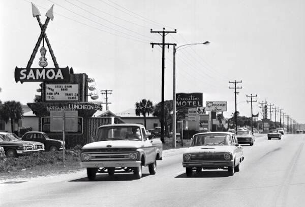 cars are driving down the street in front of some motels and palm trees on either side of the road