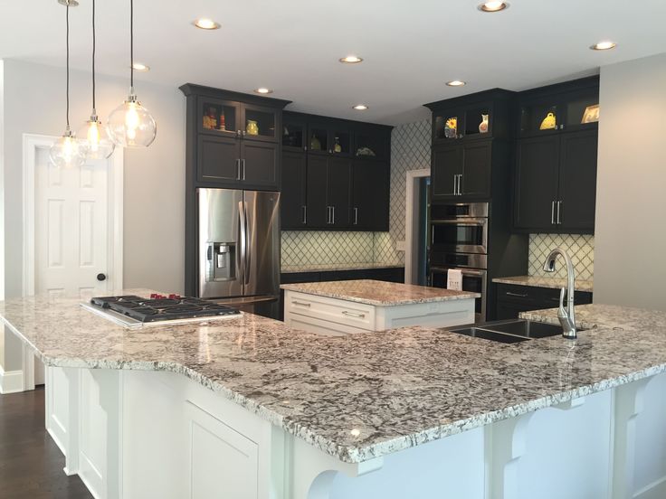 a large kitchen with marble counter tops and black cabinetry, along with stainless steel appliances