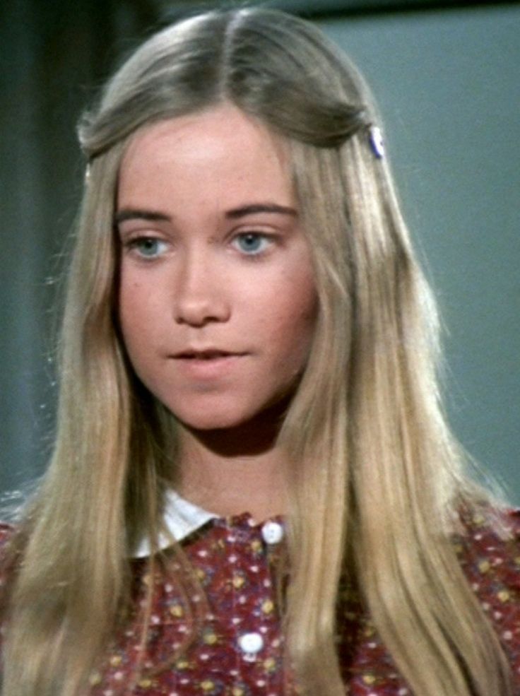 a woman with long blonde hair wearing a red shirt and white collared shirt is looking at the camera