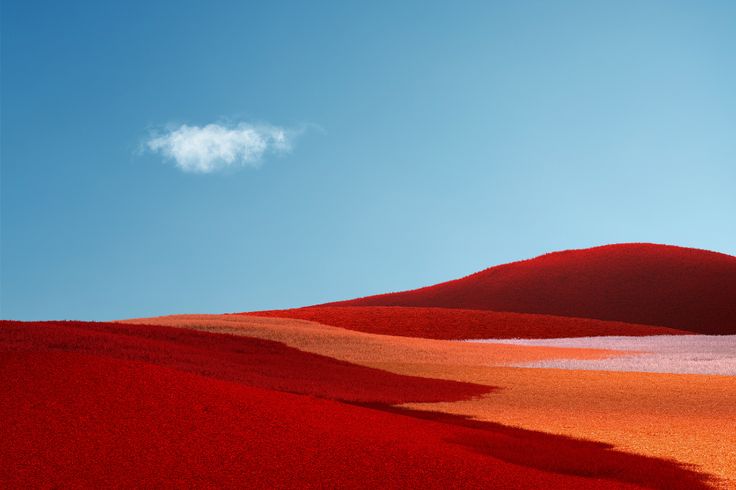 a lone cloud is in the blue sky above red hills