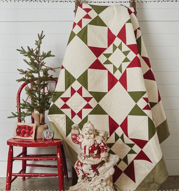 a christmas quilt hanging on a wall next to a red chair and small fir tree