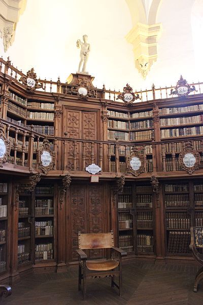 an old library with many bookshelves and clocks on the walls, along with a bench