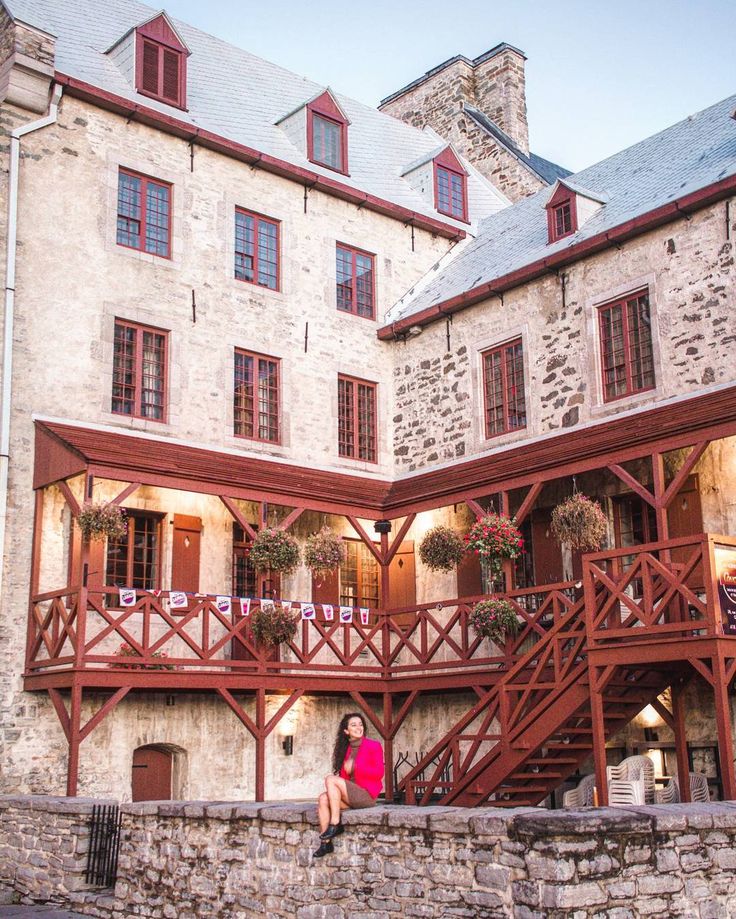 a woman is sitting on the steps in front of a stone building with red trim