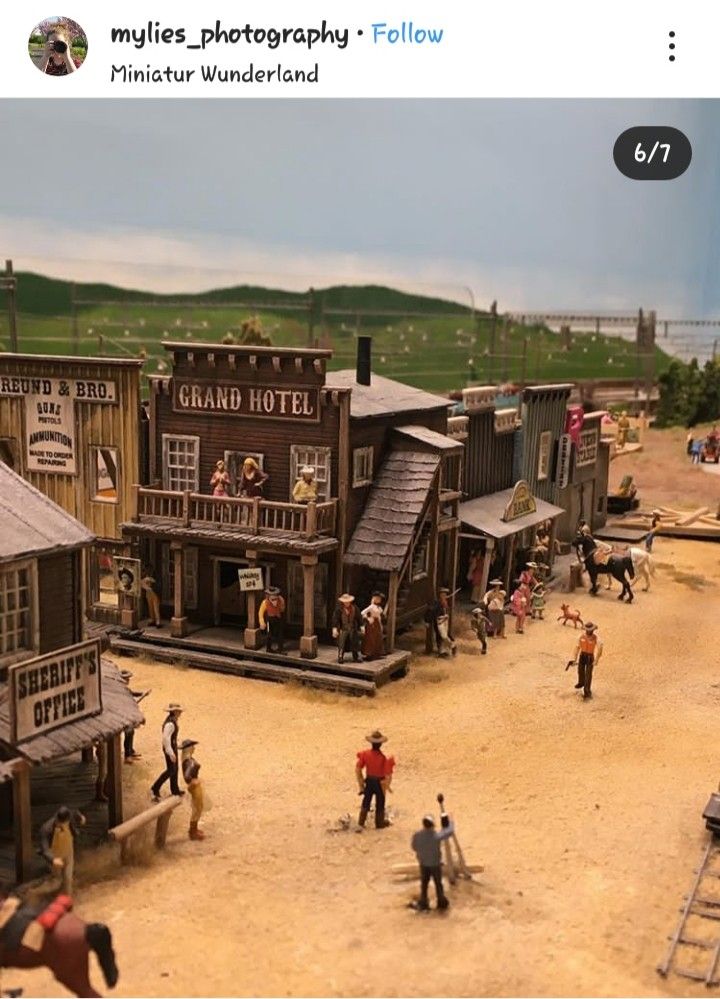 an old western town with people playing in the sand and horse drawn carriages on the road