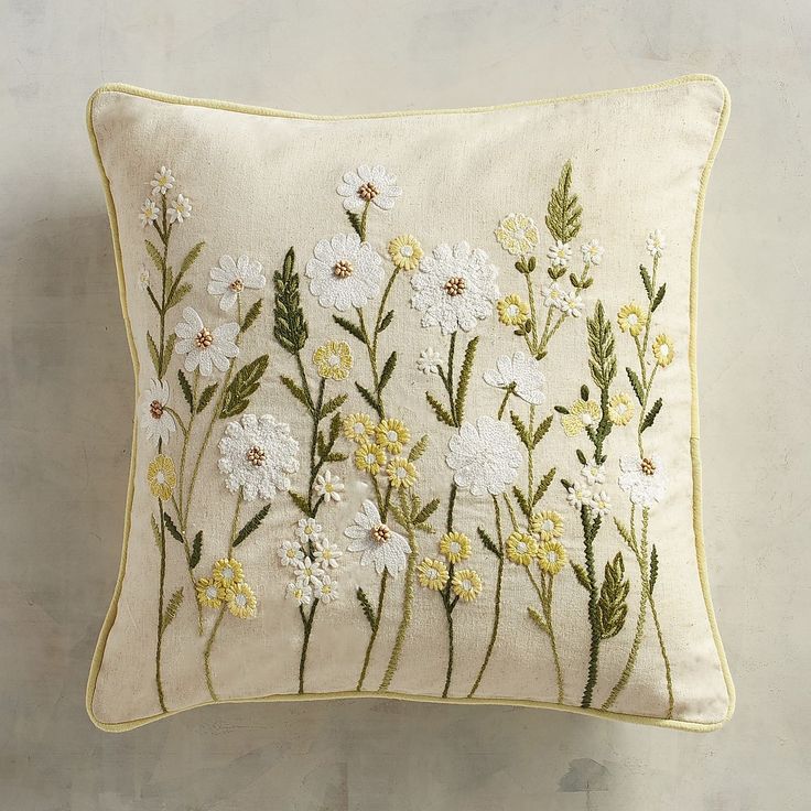 a white pillow with yellow and white flowers embroidered on the front, sitting against a wall