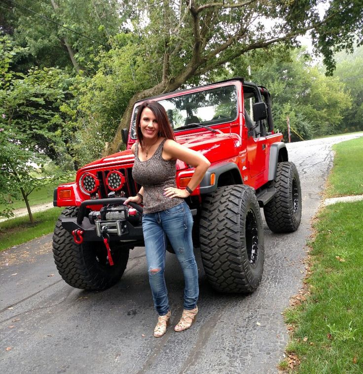 a woman standing in front of a red jeep with big wheels and huge tires on the road