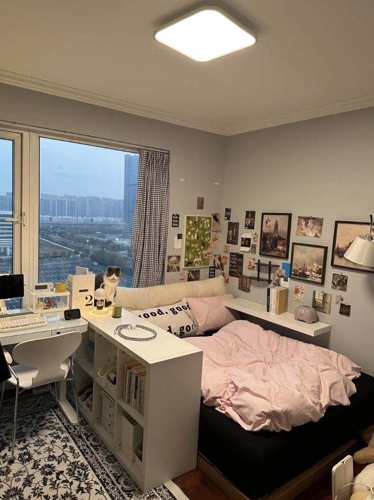 a bedroom with a bed, desk and window overlooking the city skyline in an apartment