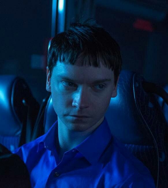 a young man in a blue shirt is sitting on a bus and looking at the camera