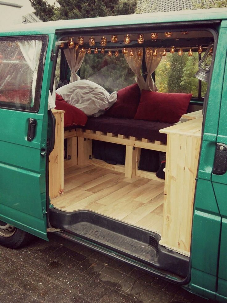 a green van with its doors open and some pillows on the bed in the back