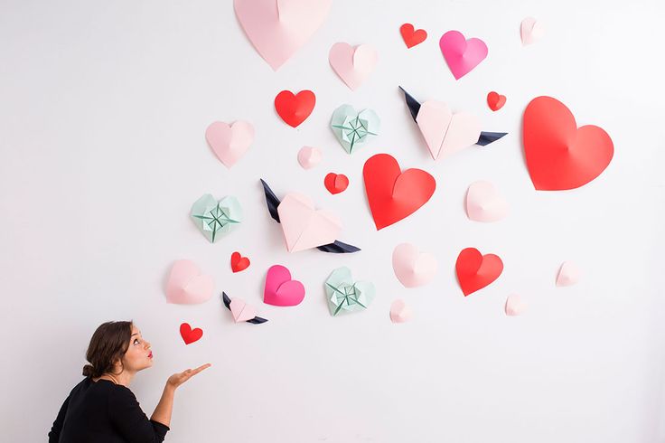 a woman standing in front of a white wall with hearts on it and one person pointing at the wall