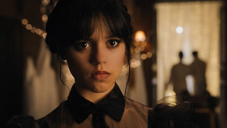 a woman with dark hair wearing a black bow tie and brown shirt in a dimly lit room