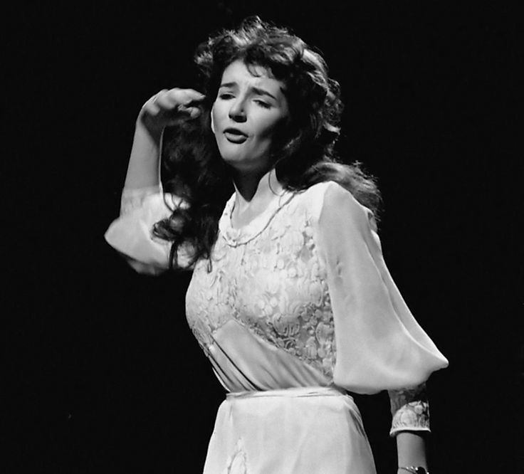 a black and white photo of a woman in a dress on stage with her hands behind her head