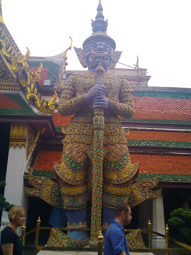 a man standing next to a statue in front of a building with gold and green decorations