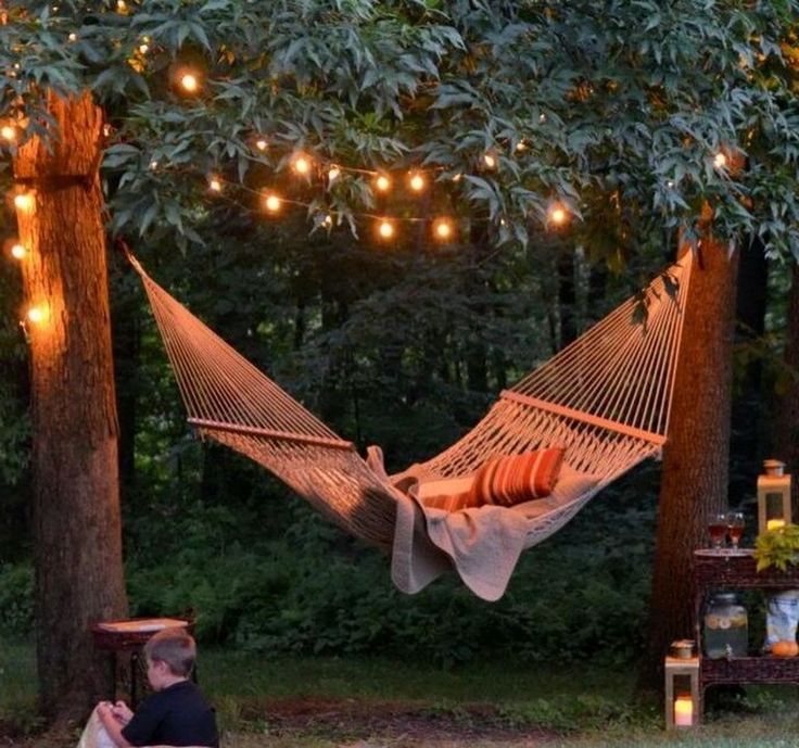 a hammock with lights hanging from it and two people sitting on the ground