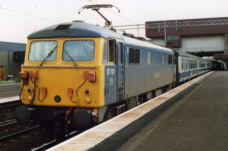 a yellow and blue train is on the tracks near a platform with an overpass