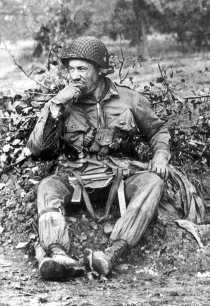 an old black and white photo of a man sitting on the ground in front of bushes