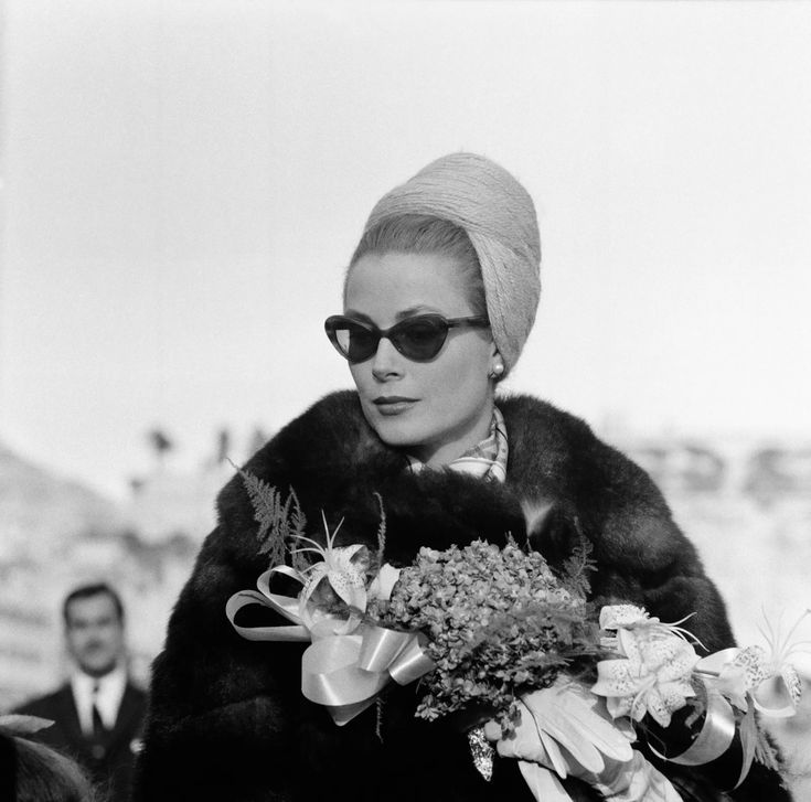 an old photo of a woman walking down the street with flowers in her hand and a man behind her