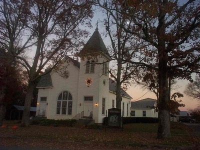 a white church with a steeple surrounded by trees and leaves on the ground at dusk