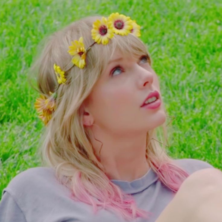 a woman laying in the grass with sunflowers on her head and looking up