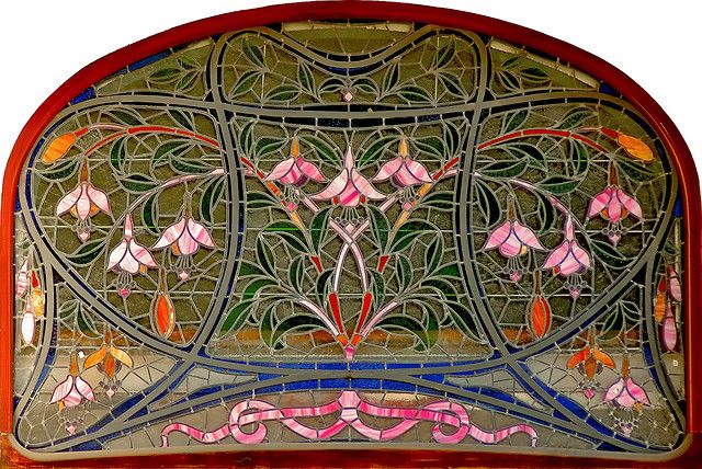 an old stained glass window with pink flowers and leaves on it's sides,