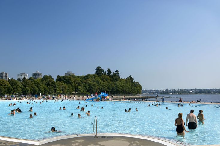 many people are swimming in a large pool with blue water and trees on the other side