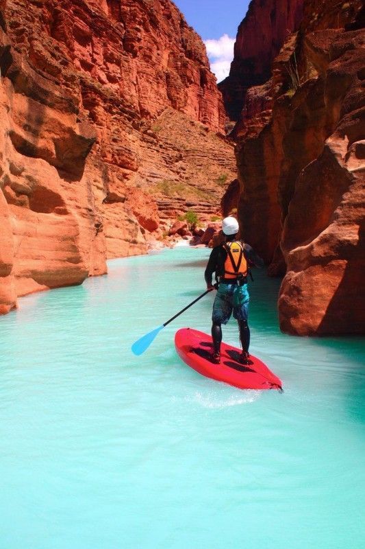 a man in a kayak paddles through the blue water between red rocks and cliffs