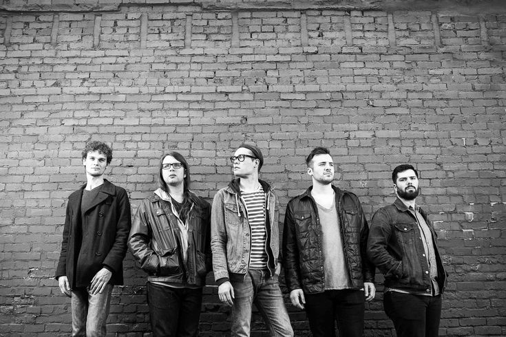 four men standing in front of a brick wall