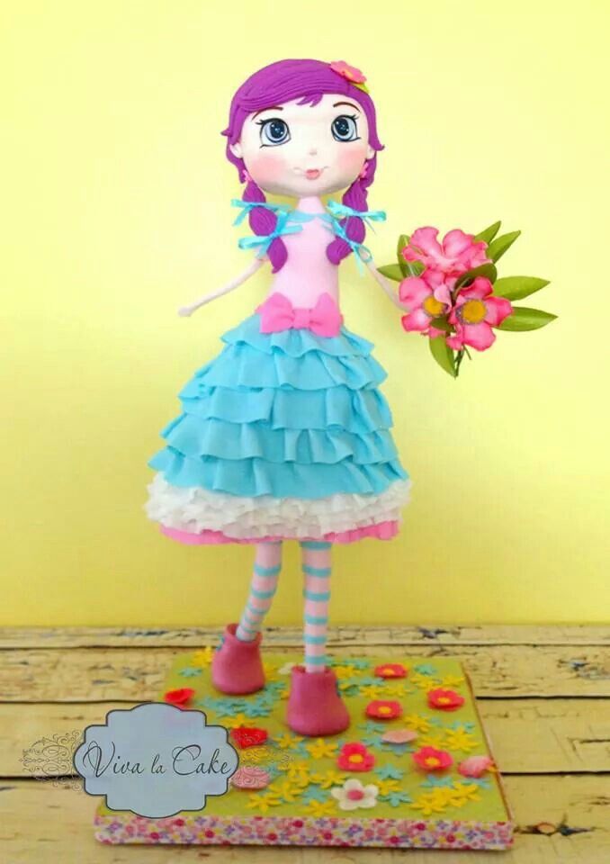 a doll is holding a bouquet of flowers on top of a card board with a yellow wall in the background