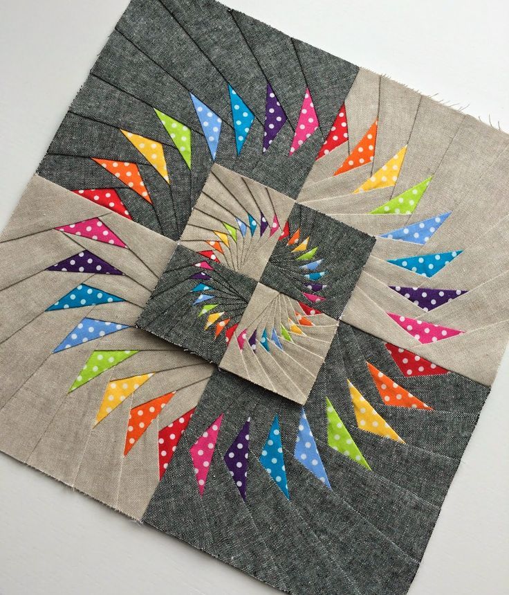 a quilted patchwork piece with multicolored arrows in the center on a white surface