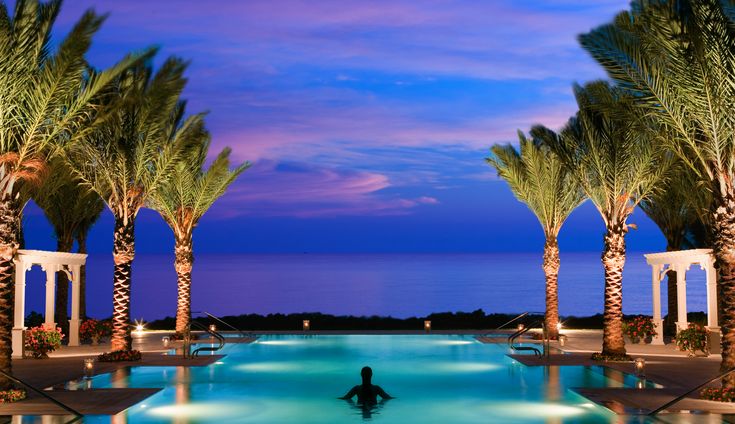 a person sitting in the middle of a swimming pool surrounded by palm trees at night