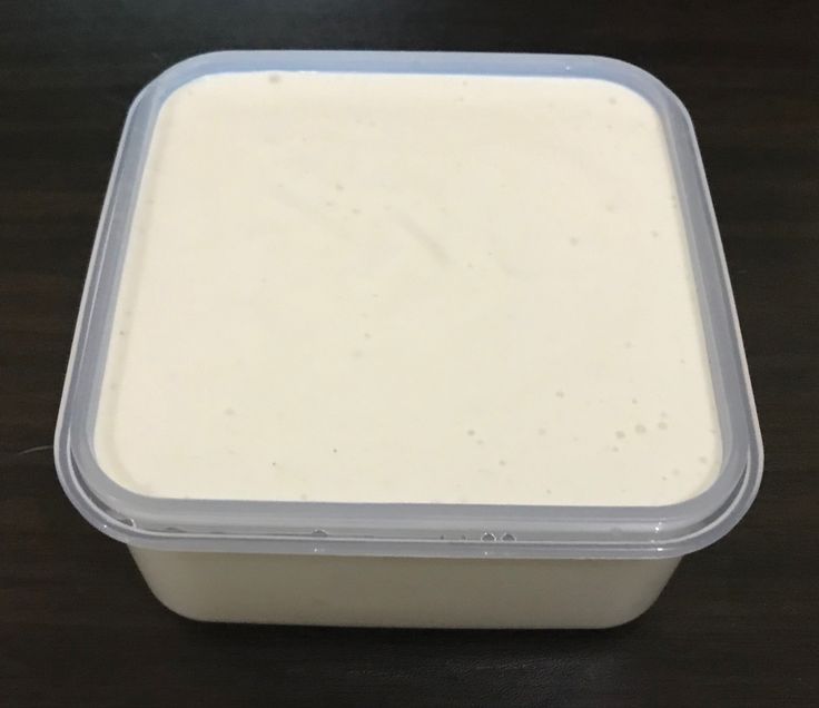 a plastic container filled with white sauce on top of a wooden table