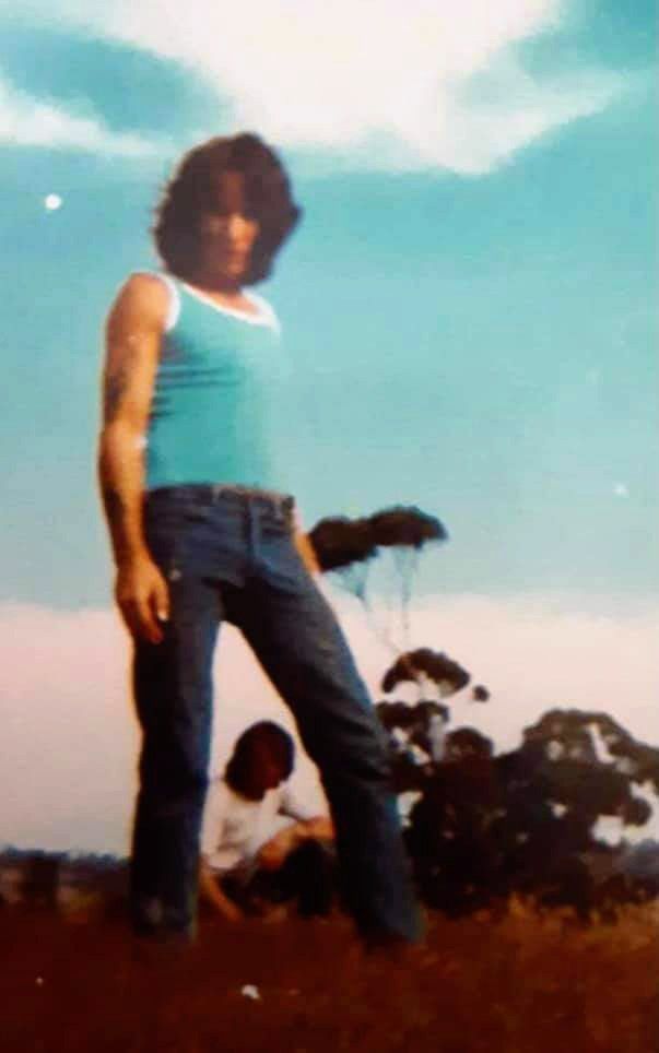 a woman standing on top of a grass covered field next to a man sitting down