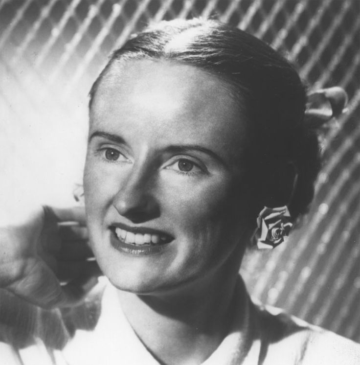 black and white photograph of a woman with large earrings on her head, smiling at the camera