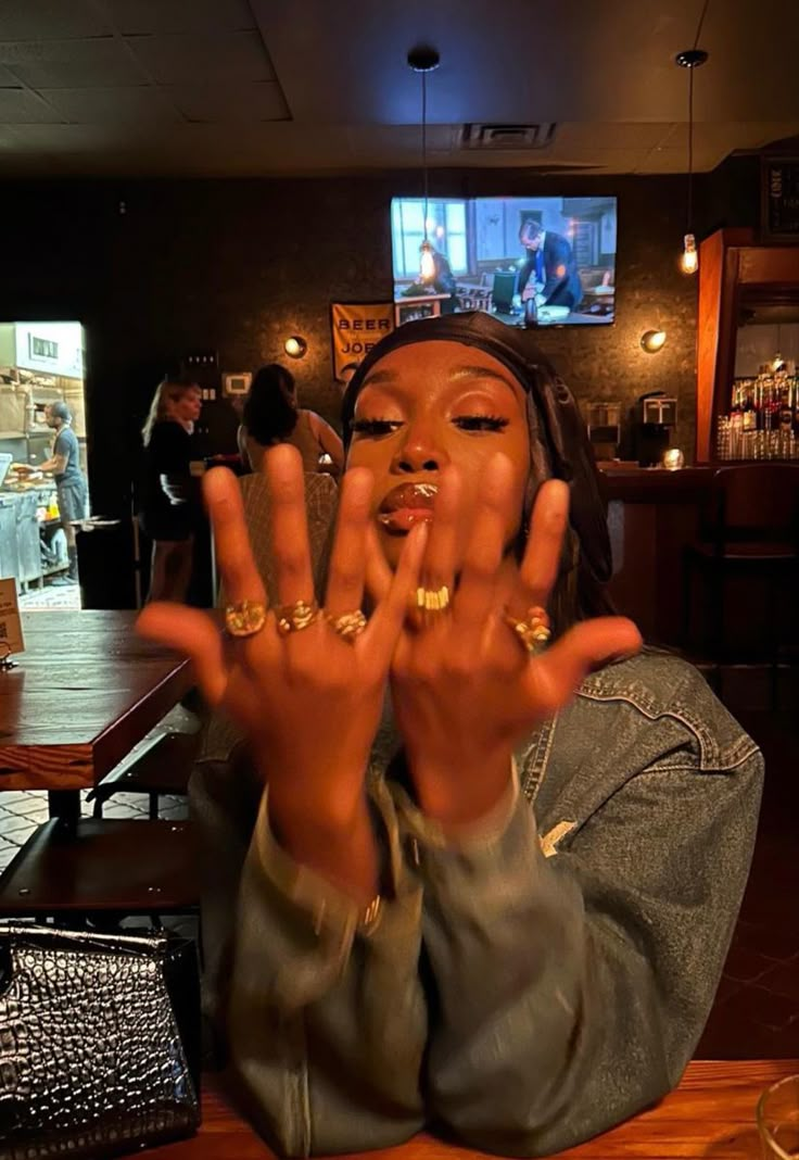 a woman sitting at a table with her hands in front of her face and fingers out