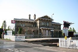 an old brick building with a white picket fence around it and a train track in front of it