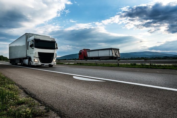 two semi trucks driving down the highway under a cloudy sky with mountains in the background