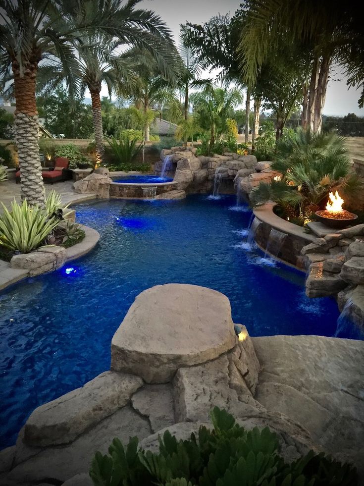 an outdoor pool surrounded by palm trees and water features a fire pit in the middle