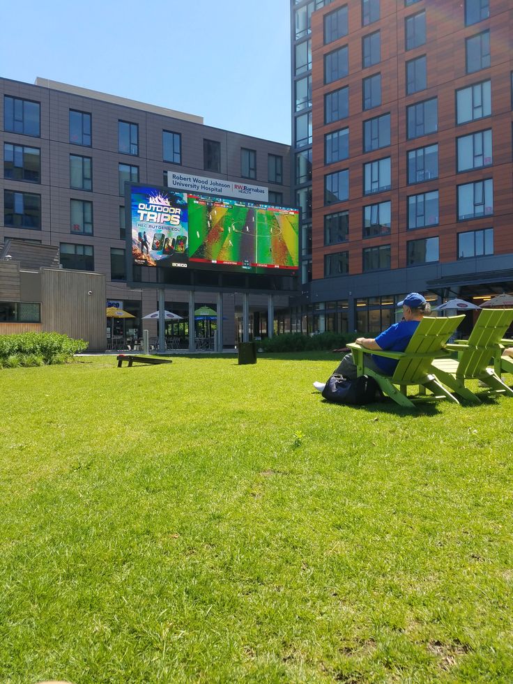 two green lawn chairs sitting in front of a building with a large screen on it