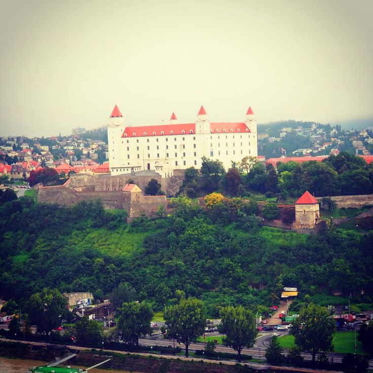 a large white building sitting on top of a lush green hillside next to a river