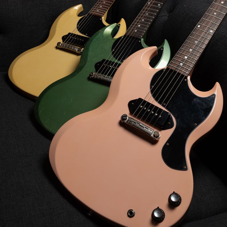 three electric guitars sitting side by side on a black surface, one is green and the other is yellow