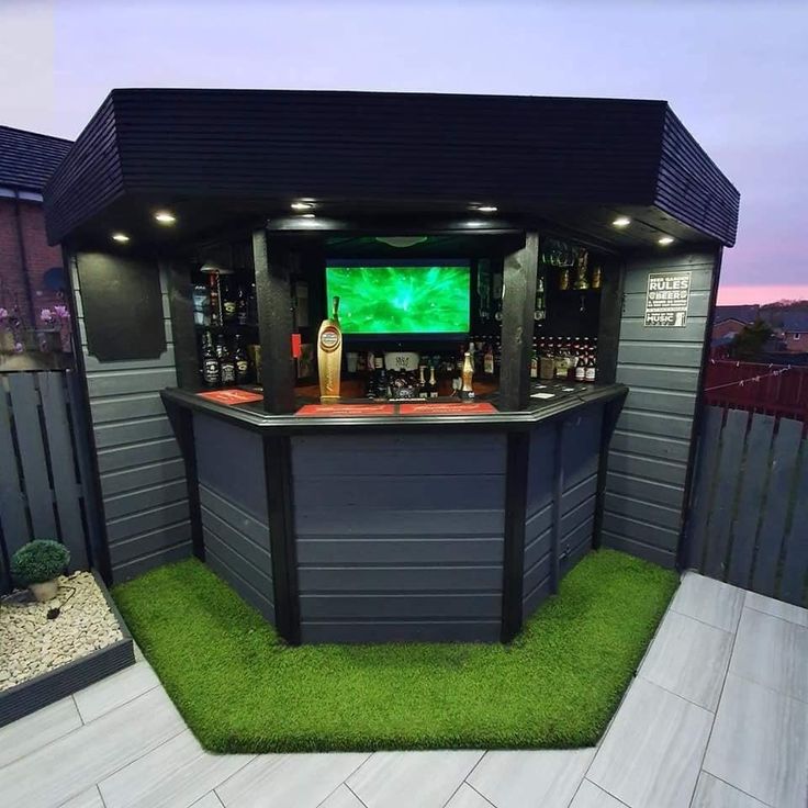 an outdoor bar with artificial grass and lights on the outside, in front of a fence