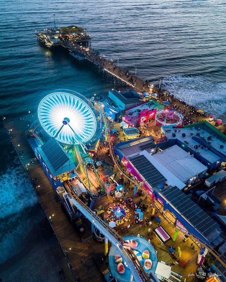 an aerial view of the fairground at night with ferris wheel, rides and water