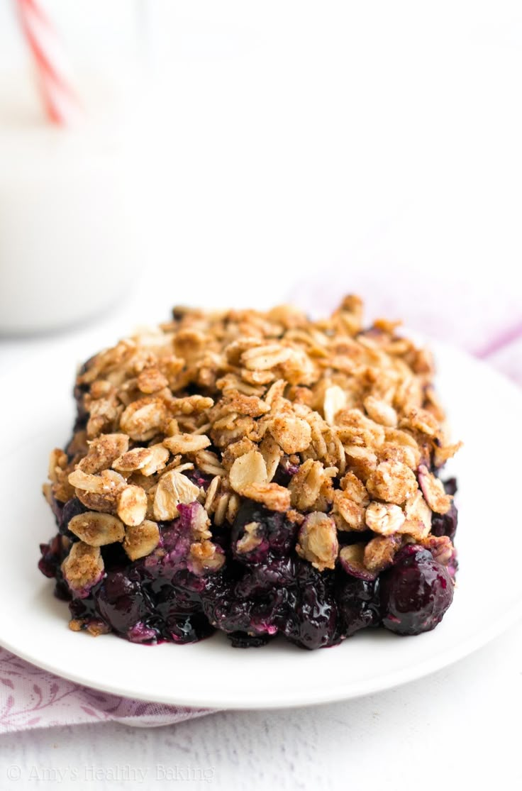 a white plate topped with blueberry crumbles next to a glass of milk