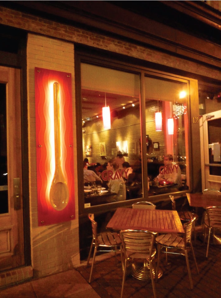 people sitting at tables in front of a restaurant with large glass doors and red lights